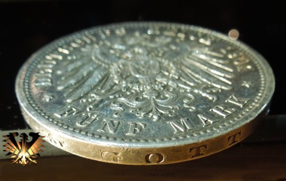 Detailansich vom Rand der Fünf Mark Silbermünze aus dem deutschen Kaiserreich. Der Rand ist Glatt und trägt die Inschrift: GOTT MIT UNS.